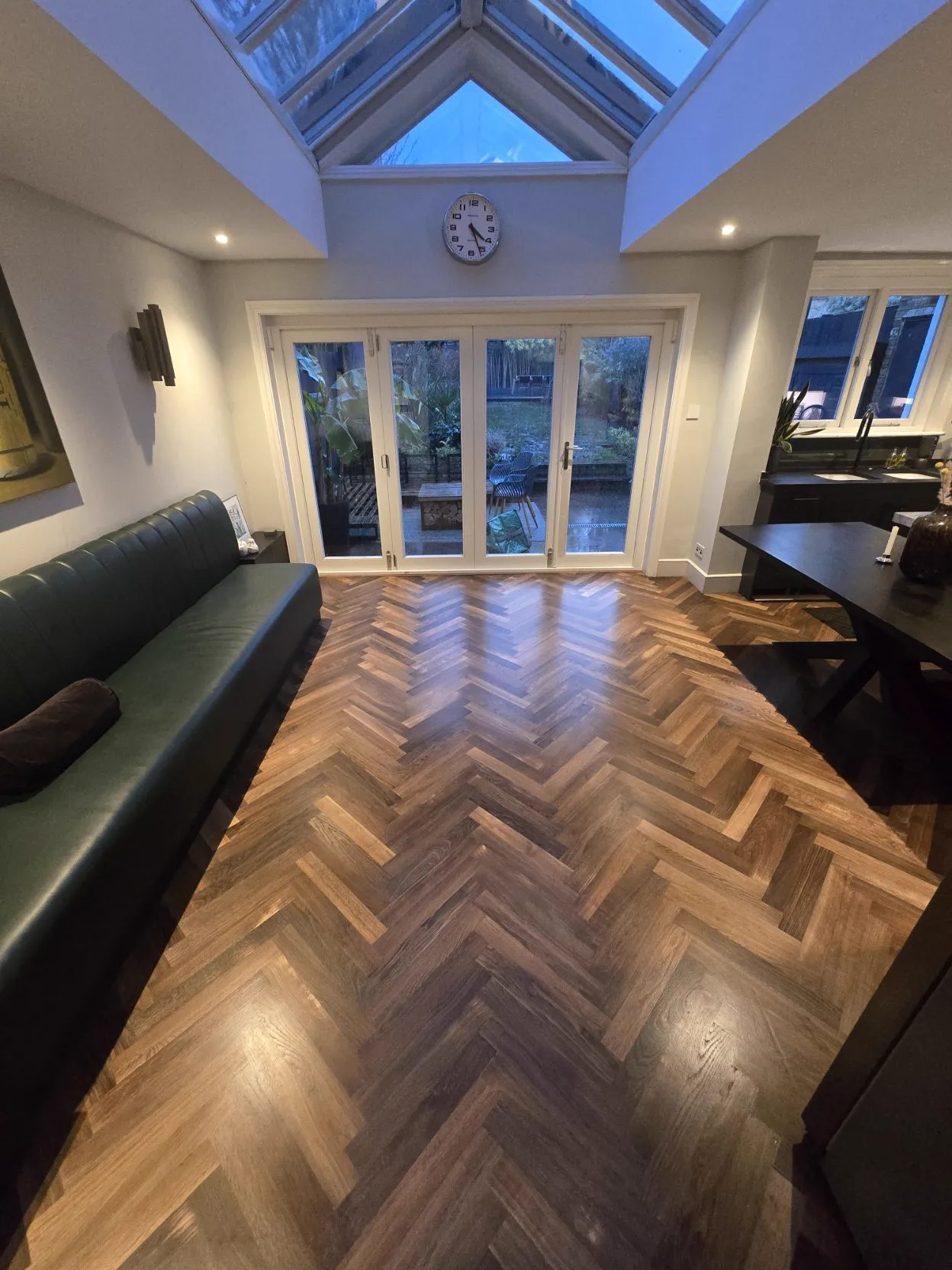 Oak herringbone parquet meeting dark plank flooring in a snug with green leather seating, by Howard Naish