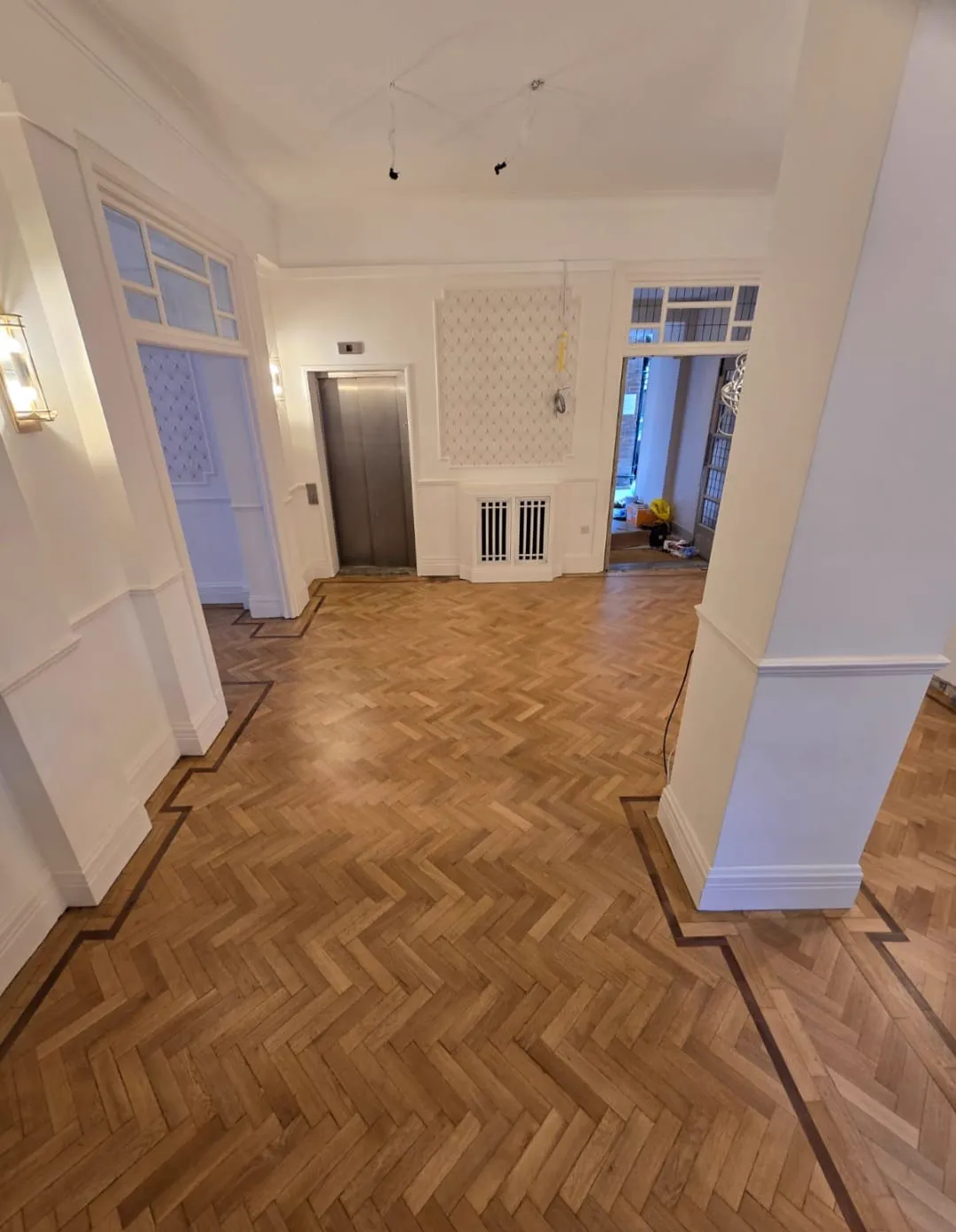 Restored herringbone parquet with a dark border in a Chelsea apartment block reception, by Howard Naish